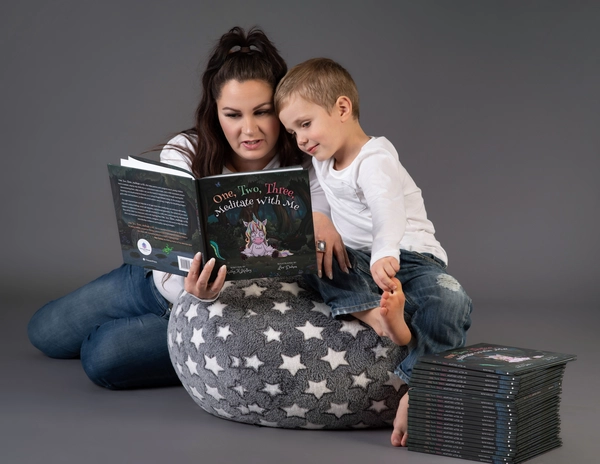IMGP8252 (1) A parent sits on a plush rug, reading a children's book titled "One, Two, Three, Meditate with Me" to a young child.